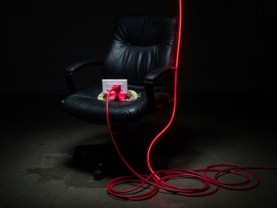 An office chair with a wall outlet growing from the seat and a neon cord on the floor.